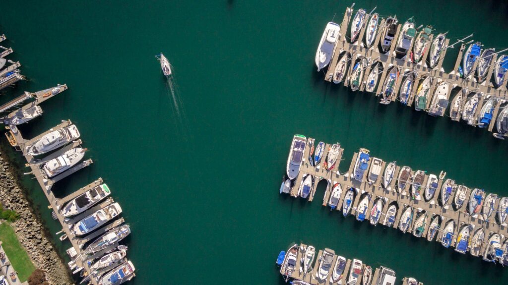 An aerial shot of a marina with neatly parked boats and a lone boat moving through the water.