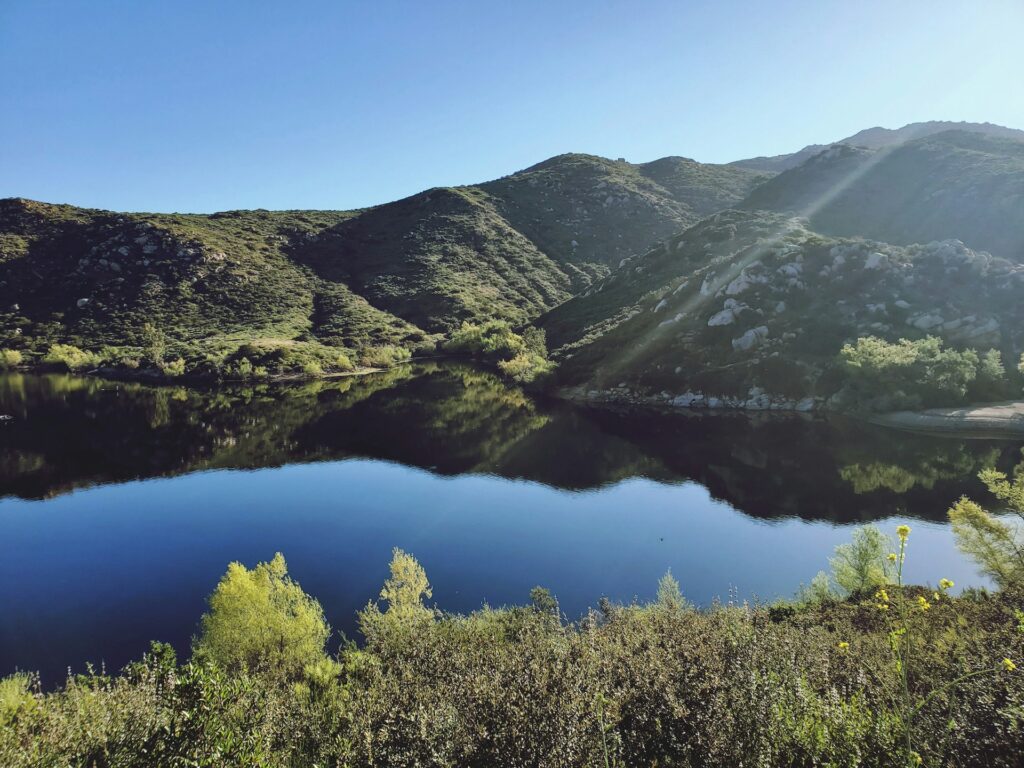 A peaceful lake surrounded by hills, with clear blue skies reflecting off the calm water.