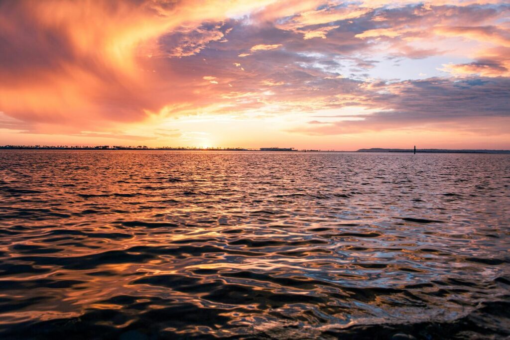 A vibrant sunset over calm ocean waters with an orange and pink sky.