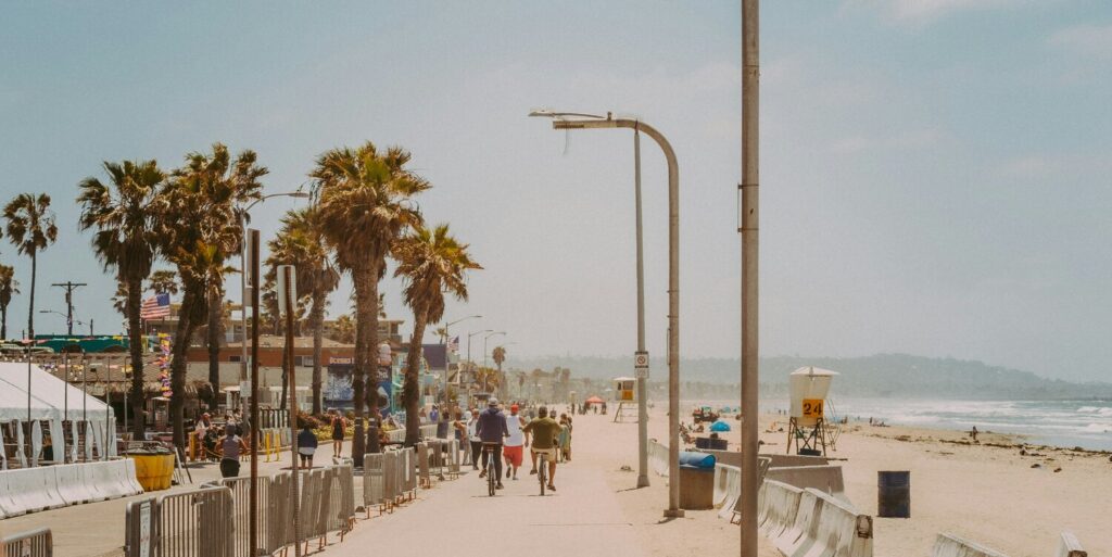 A lively beach path lined with palm trees, where people are biking and walking by the shore.