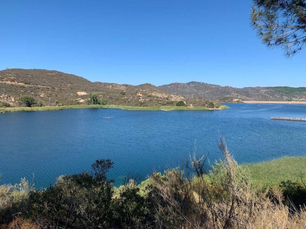 A serene lake surrounded by dry hills under a clear blue sky.