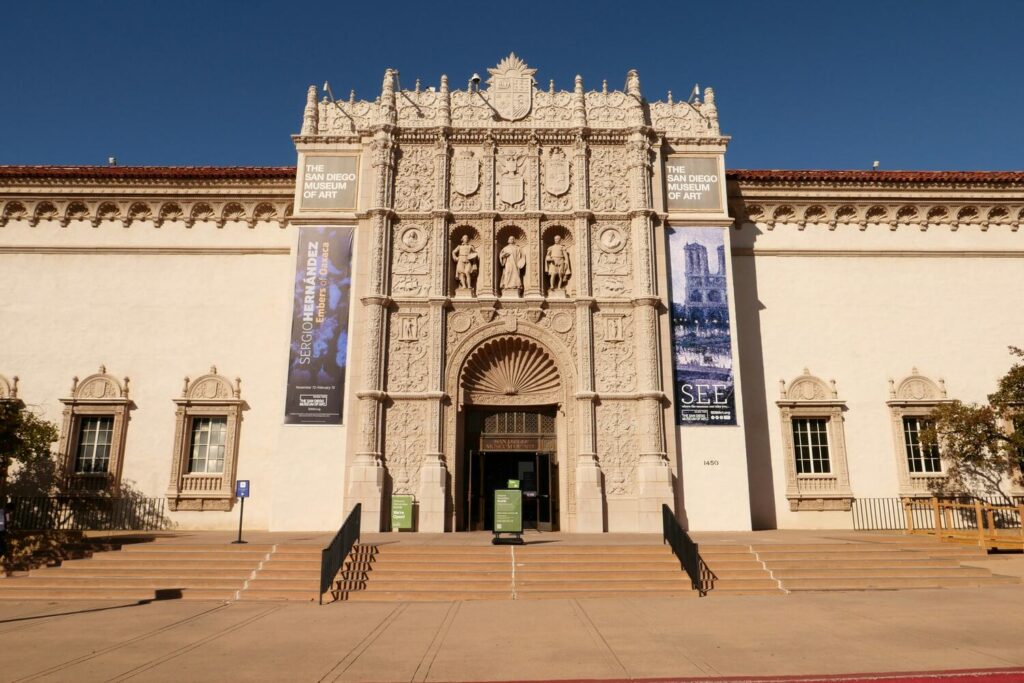 The ornate facade of The San Diego Museum of Art in Balboa Park, featuring banners for current exhibitions.