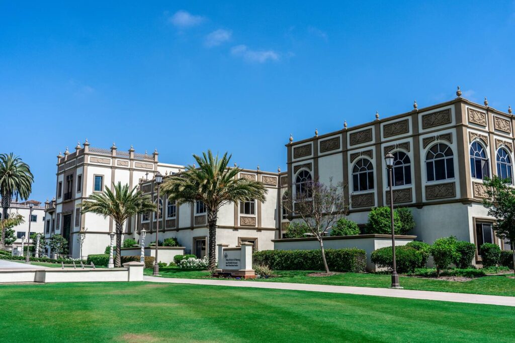 A sunny view of a historic, ornately decorated building surrounded by palm trees and green lawns under a clear blue sky.