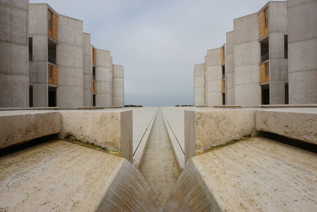 A symmetrical view of the Salk Institute's courtyard in San Diego, featuring modern concrete buildings and a central water channel leading to the horizon.