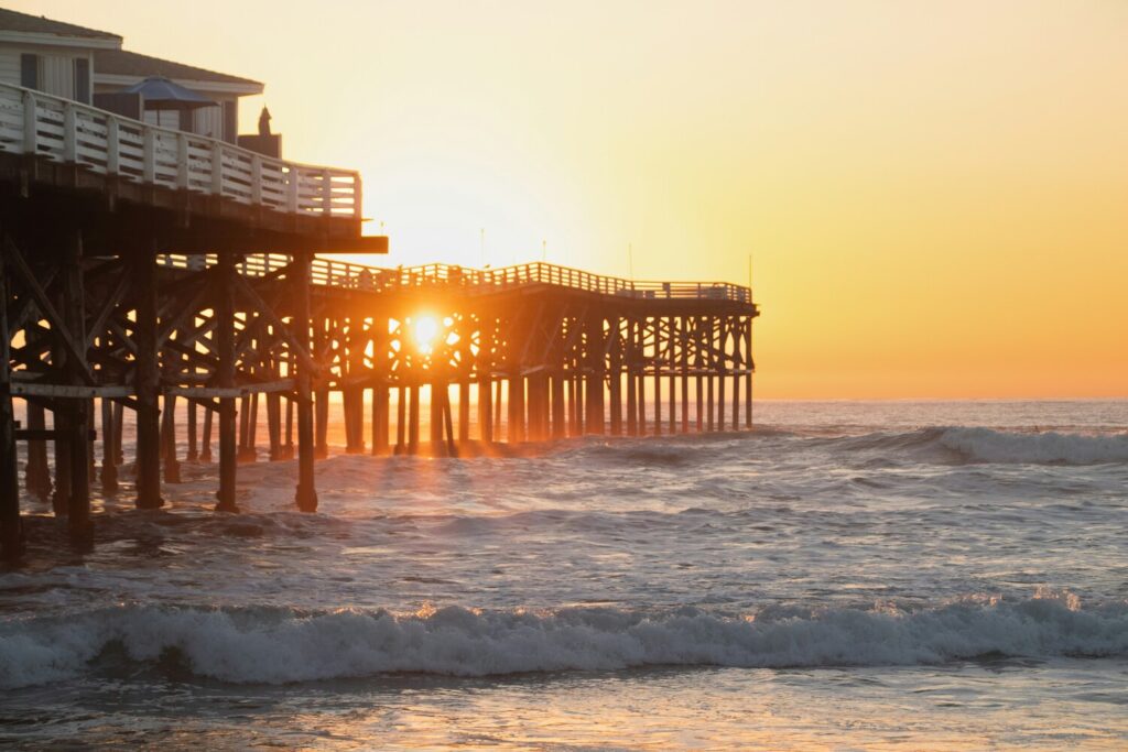 A wooden pier stretches into the ocean with the sun setting behind it, casting a golden glow.