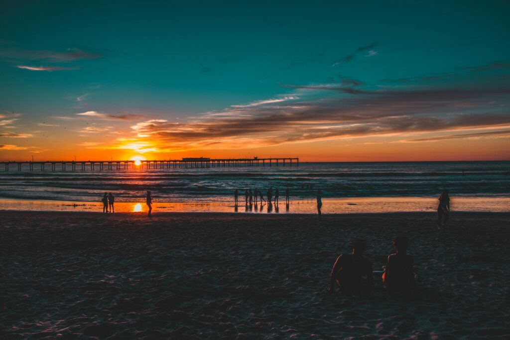 People enjoy a vibrant sunset on the beach with a pier stretching into the ocean.