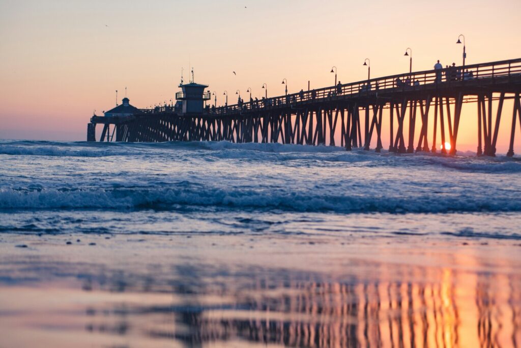 Sunset view of a long pier extending over the ocean with gentle waves and a pastel sky.