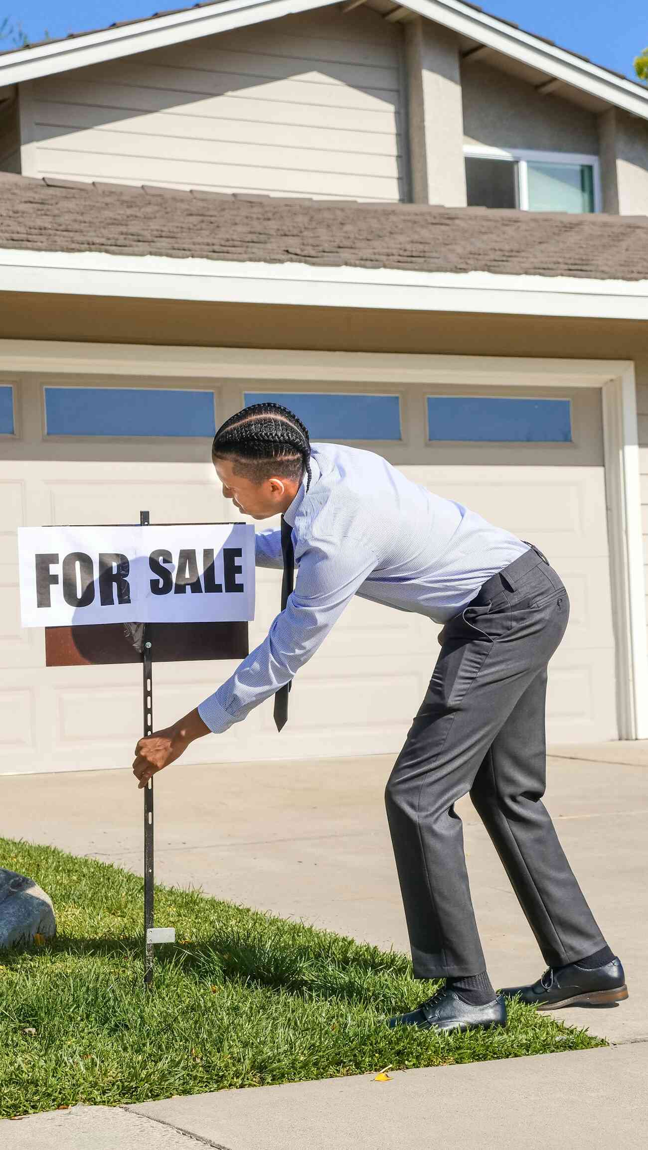 A man pushing a for sale sign in front of a house, indicating the property is available for purchase