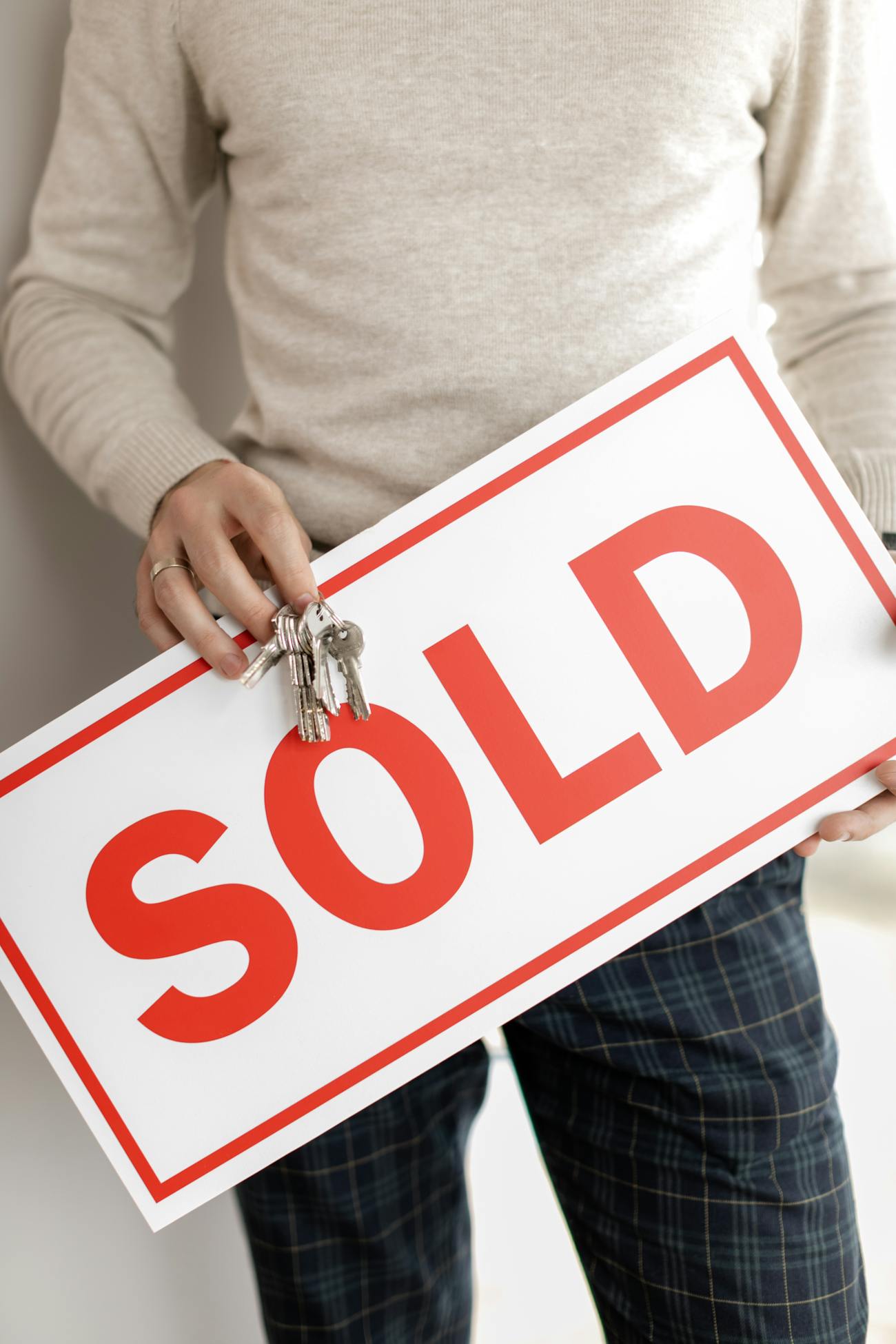 A man holding house keys and a sold sign
