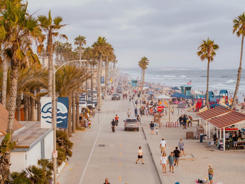 Crowded beach boardwalk lined with palm trees and people walking